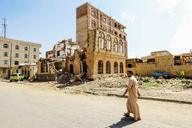 A man walks down a street in front of a destroyed building.